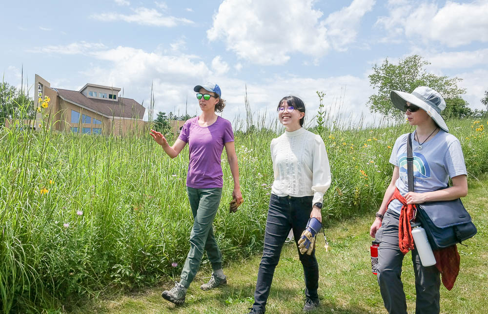 Grace and Weijiam walk through the prairie with Dr. Amy Alstad to participate in care for the earth. The monastery is in the background.