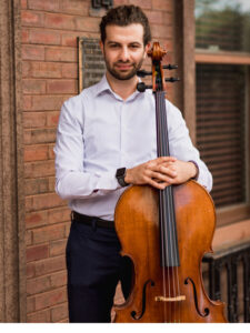 George Teague stands holding a cello